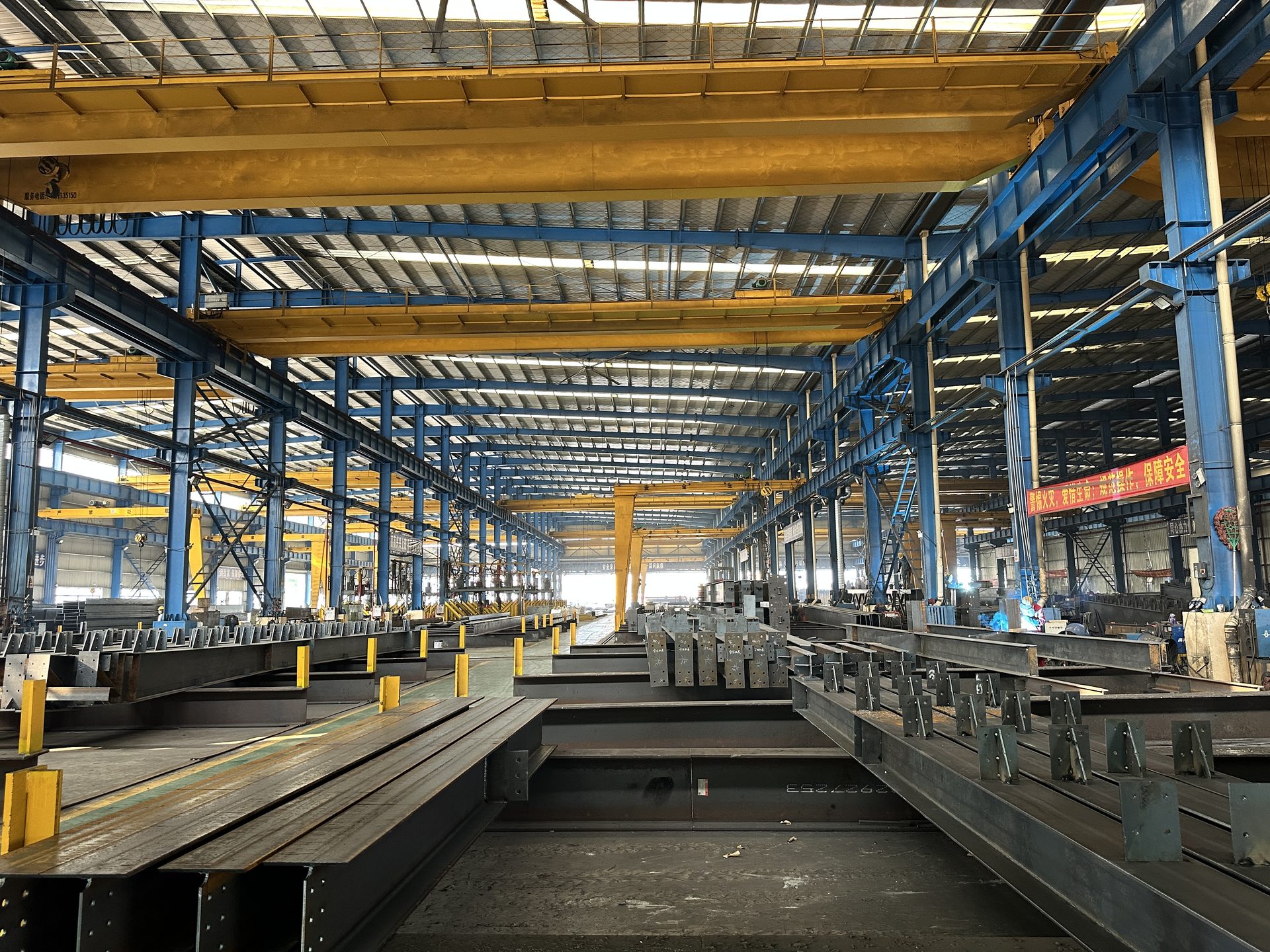 Yellow double-girder overhead cranes running on corbel runway girders inside a steel workshop