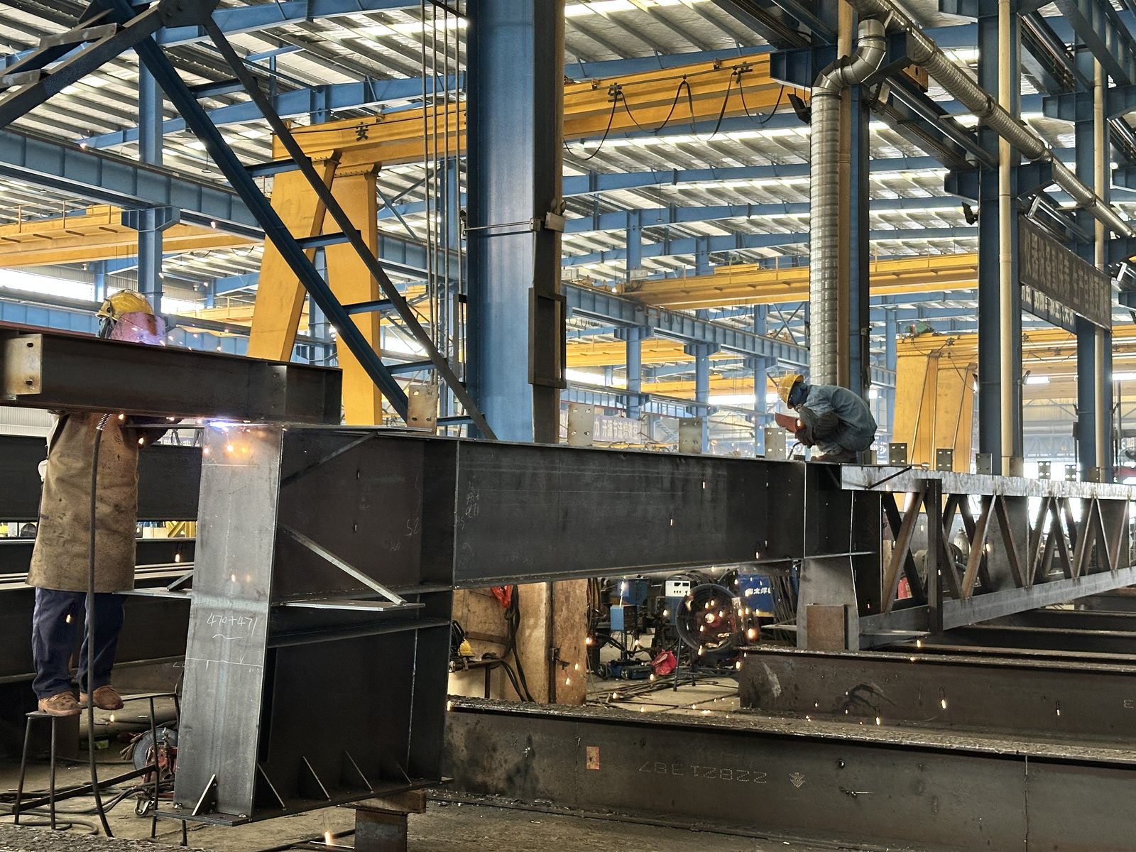 Welders assembling heavy steel members with several overhead cranes serving the bay